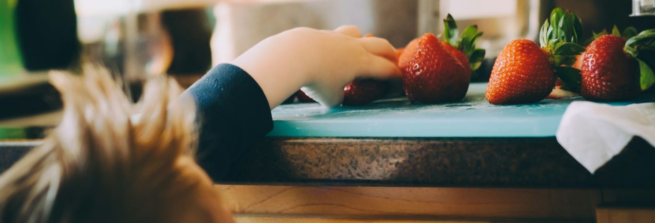 Small child reaching up onto the kitchen counter to grab a strawberry