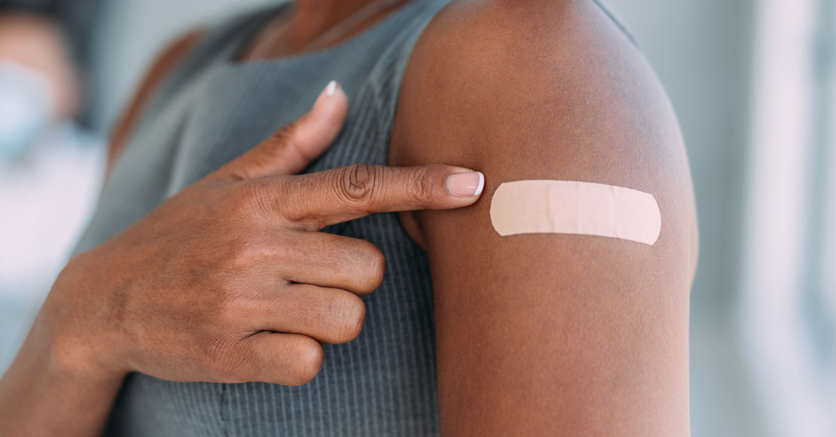 African American woman in gray tank top pointing to bandaid on her left arm