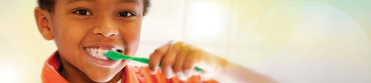 African American child in red shirt brushing teeth with green toothbrush