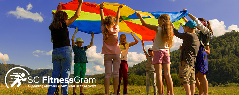 Children playing with rainbow tarp outside. SC FitnessGram logo in white in bottom left corner