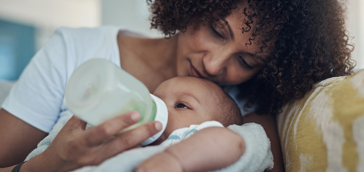 African American mom with short curly hair feeding her baby boy a bottle