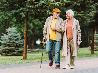An elderly couple linking arms walking in the park