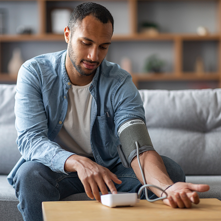 Man sitting on couch is checking his blood pressure himeself using a cuff
