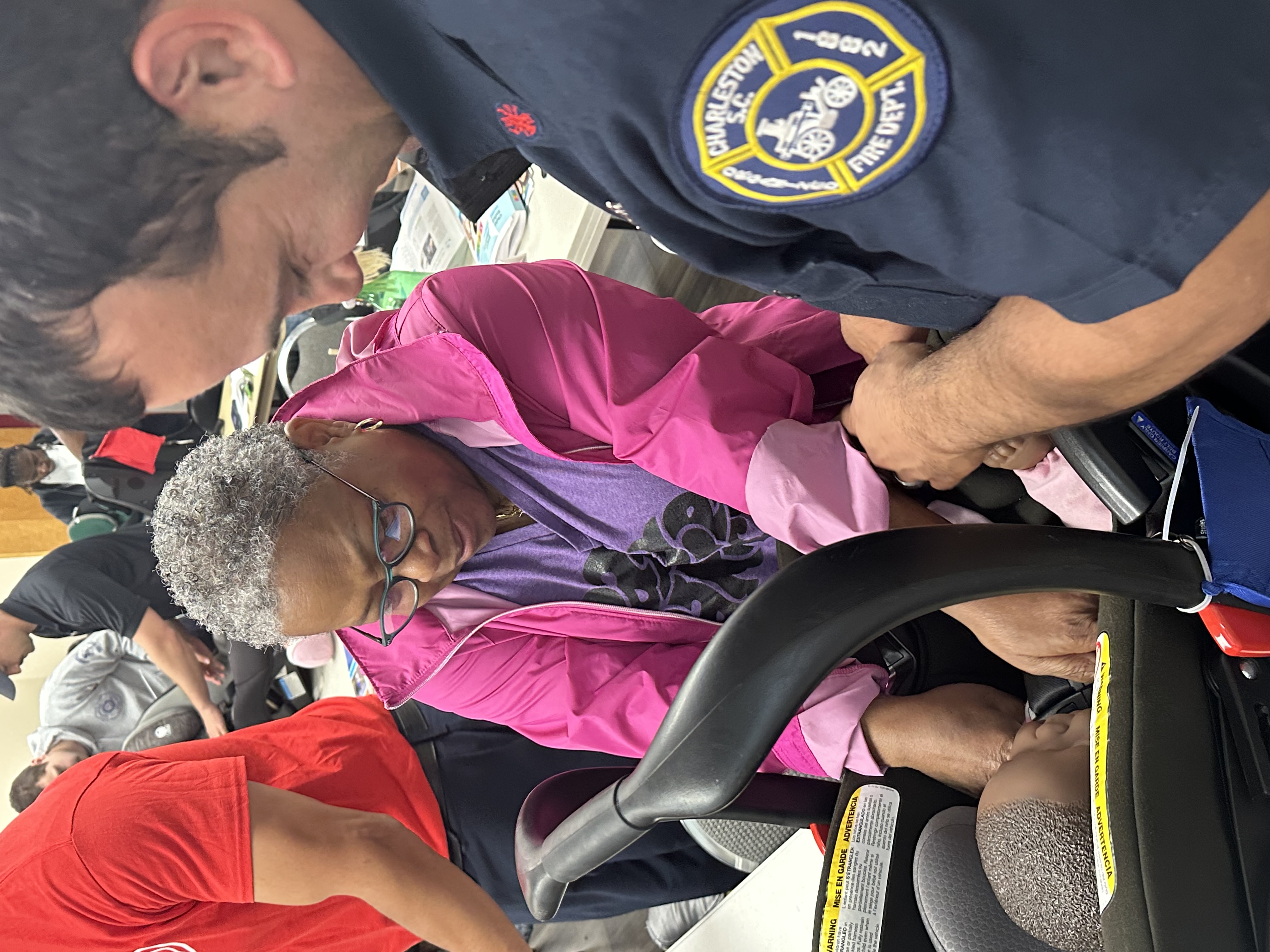 Woman and firefighter practicing fitting a baby doll into car seat.