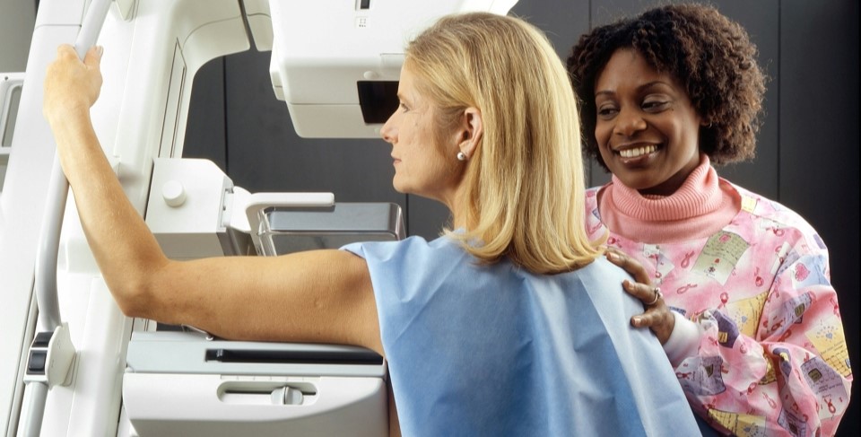 Older, blonde female patient wearing hospital gown is being screened for cancer. She has her arm on the screening machine